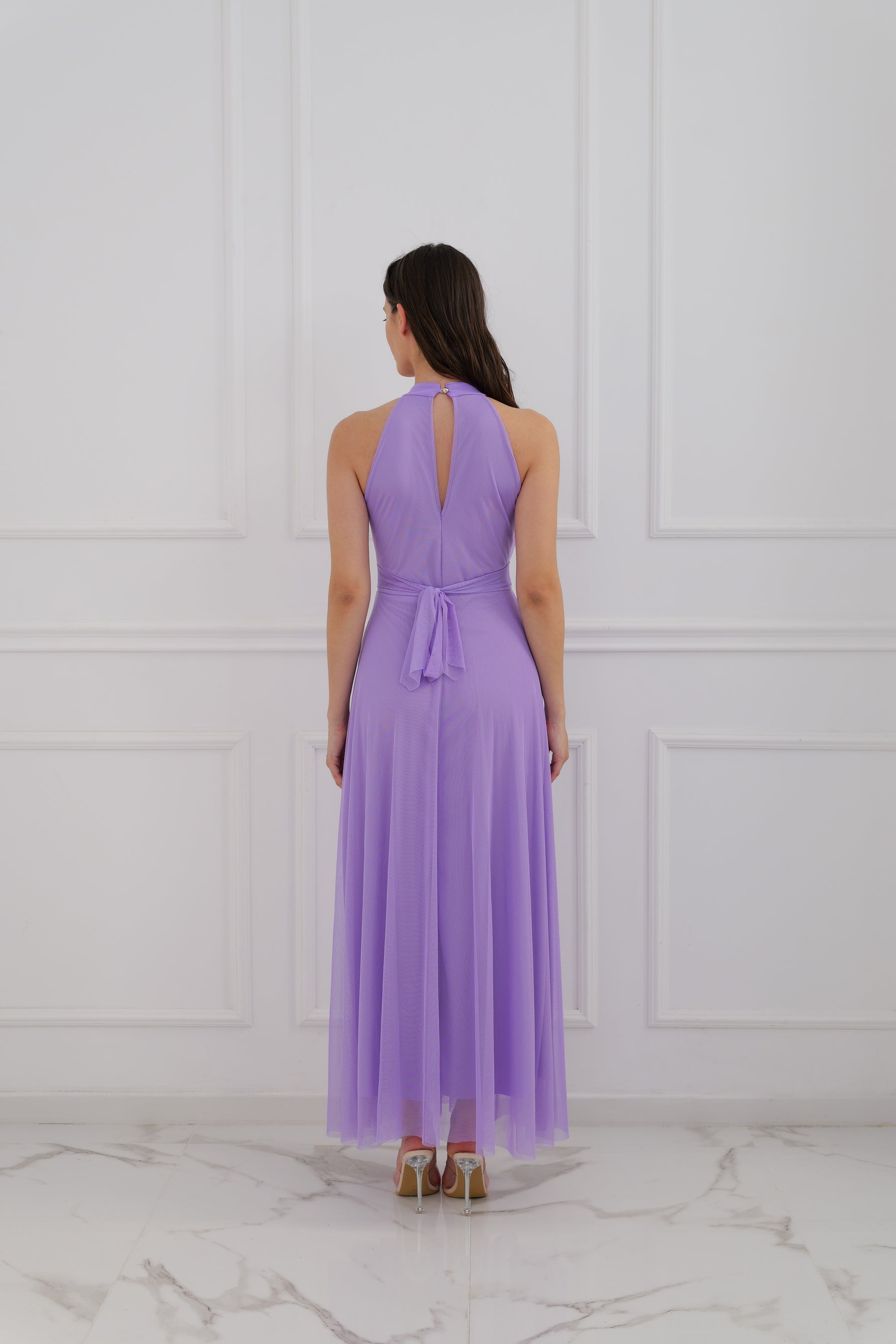 Abito lilla a halter, donna in posa elegante, pianta verde decorativa