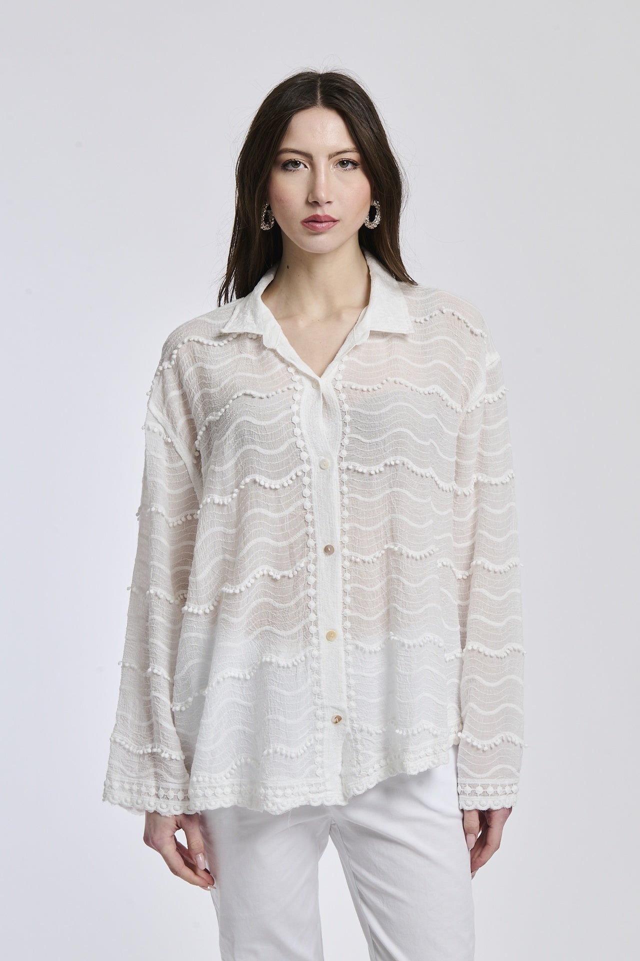 Donna in abbigliamento estivo: camicia bianco a uncinetto e pantaloni bianchi, posa stilosa