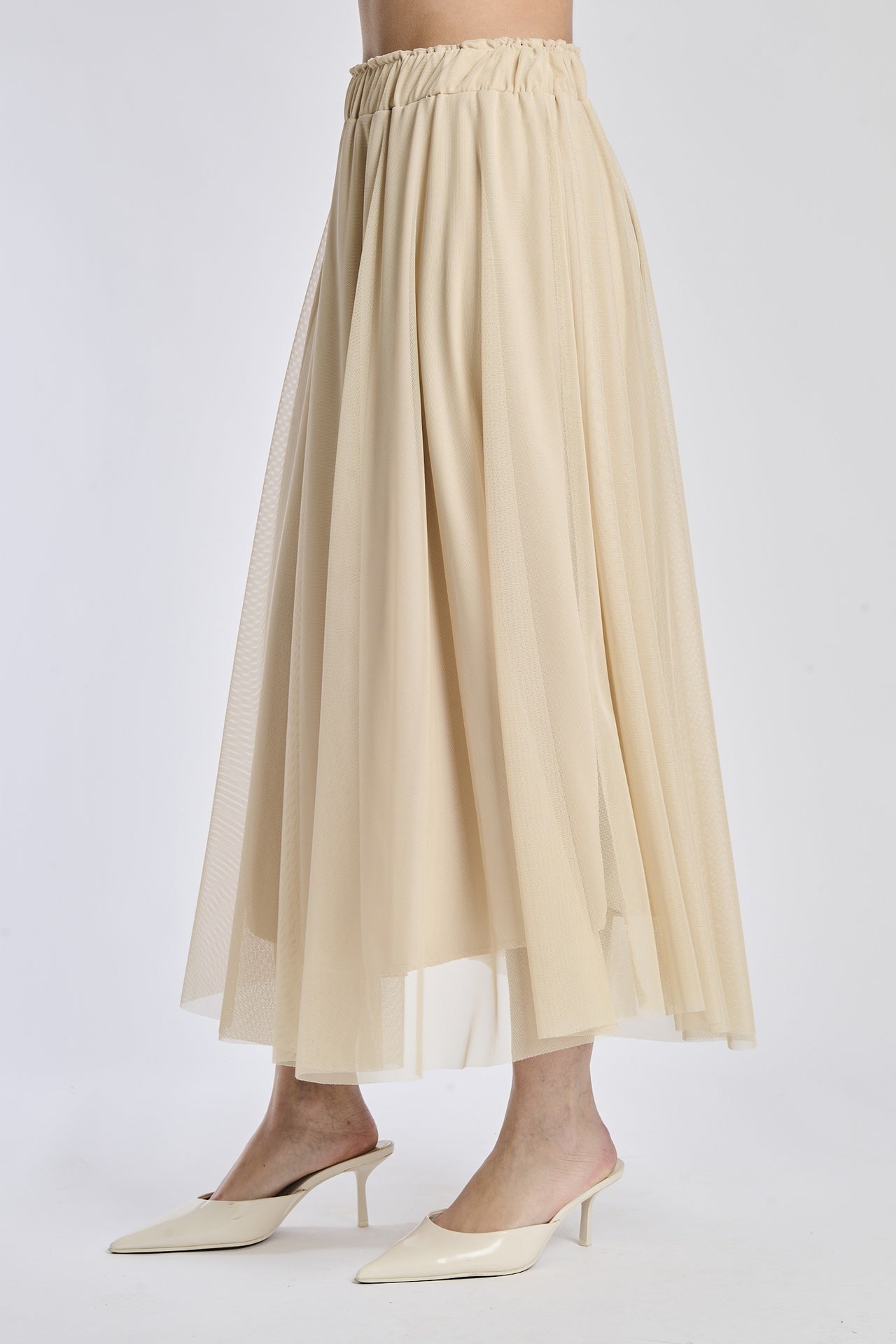Gonna lunga in tulle beige, vita elastica, abbinata a sandali alti.
