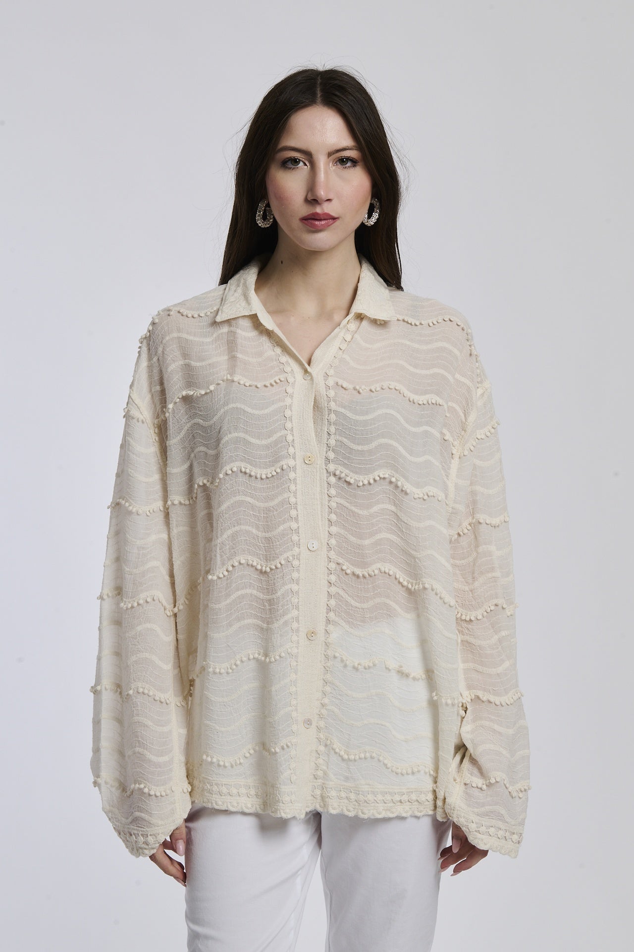 Donna in abbigliamento estivo: camicia beige a uncinetto e pantaloni bianchi, posa stilosa