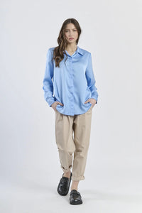 Camicia azzurra in seta con colletto, abbinata a pantaloni beige.