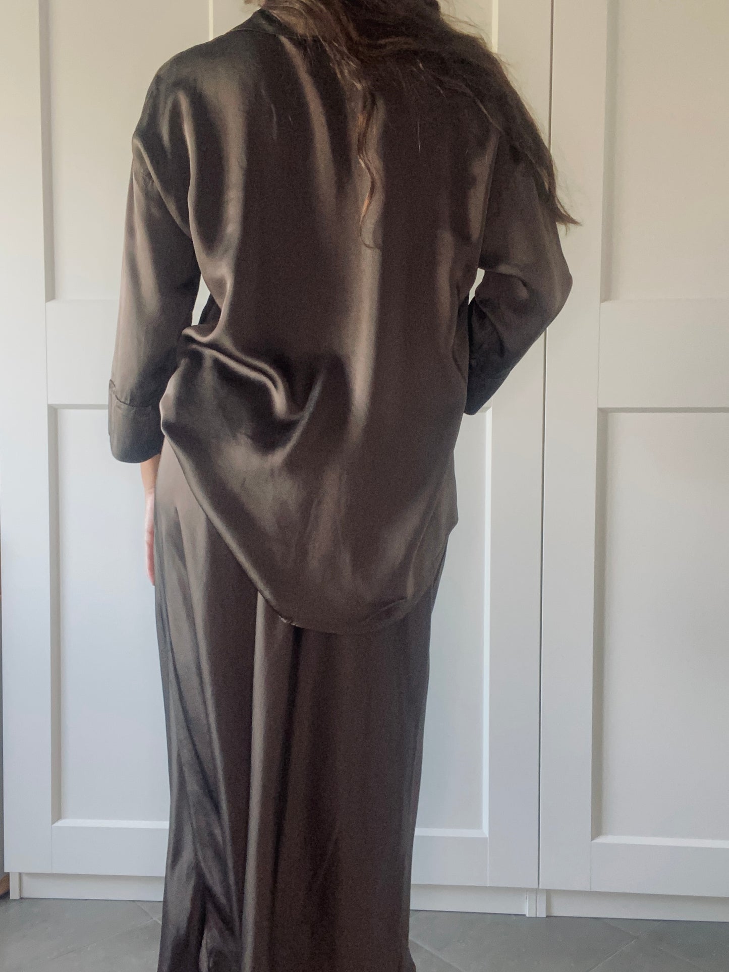 Completo in seta fango per donna: camicia a bottoni e gonna slit, modello con posa naturale davanti a porte bianche.