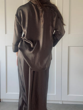 Completo in seta fango per donna: camicia a bottoni e gonna slit, modello con posa naturale davanti a porte bianche.