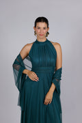 Donna con abito elegante di colore verde scuro, collo alto a imbarcatura, gonna lunga, con foulard in tulle trasparente, su sfondo chiaro.

