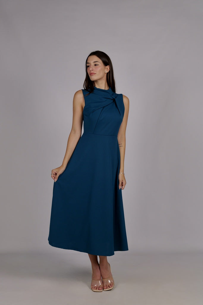 Donna con abito ottanio senza maniche, midi, con nodo decorativo al petto, look elegante.