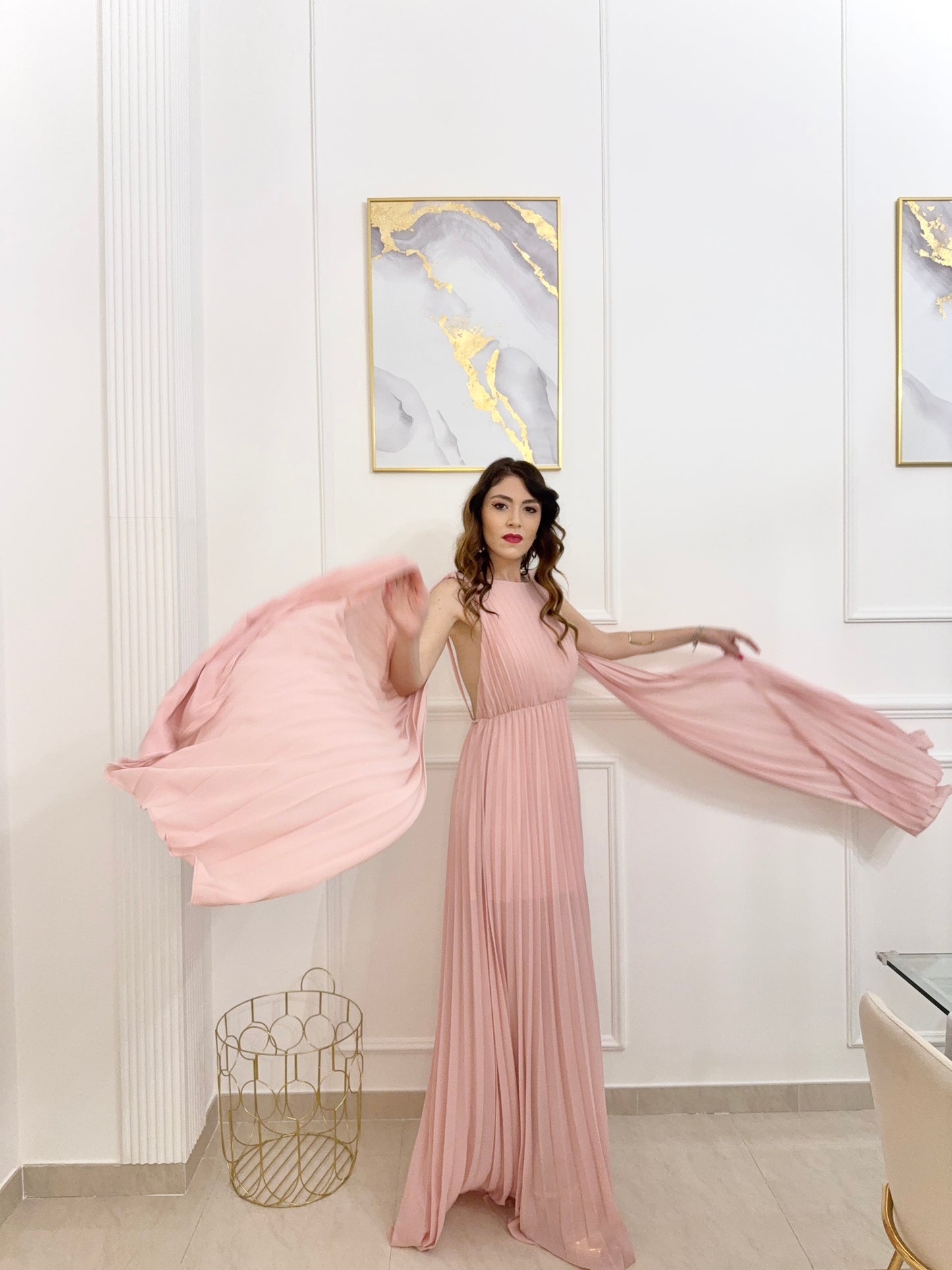 Donna con abito rosa plissé e mantelle, posa sul lago con montagne