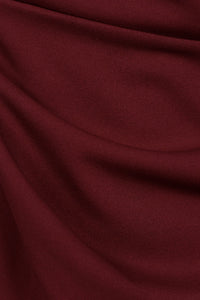 Donna indossa un abito bordeaux senza maniche, lunghezza midi, con nodo al petto, look raffinato.
