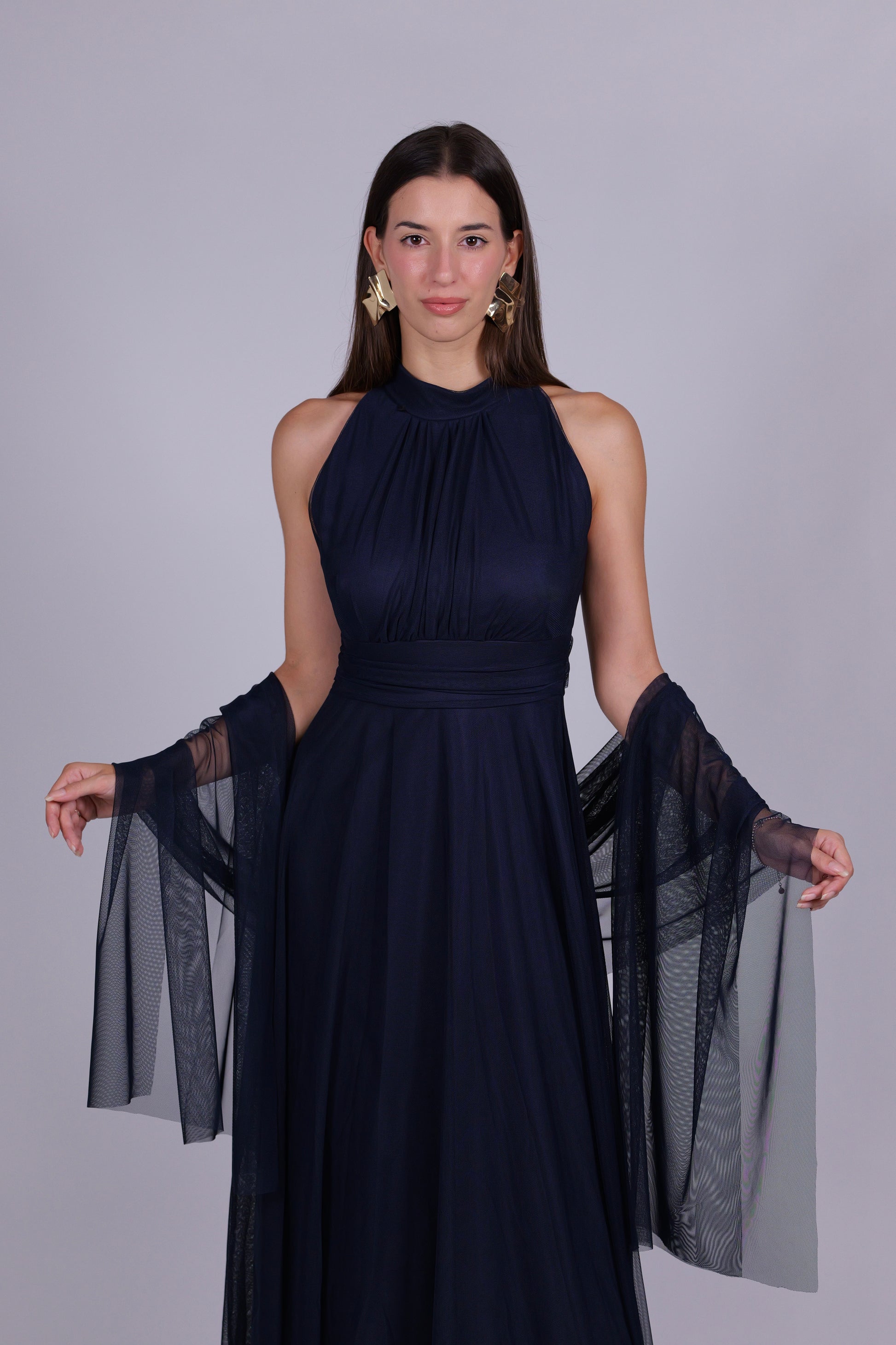 Donna indossa un abito navy elegante, collo a imbarcatura, gonna lunga, con foulard in tulle trasparente, look elegante.