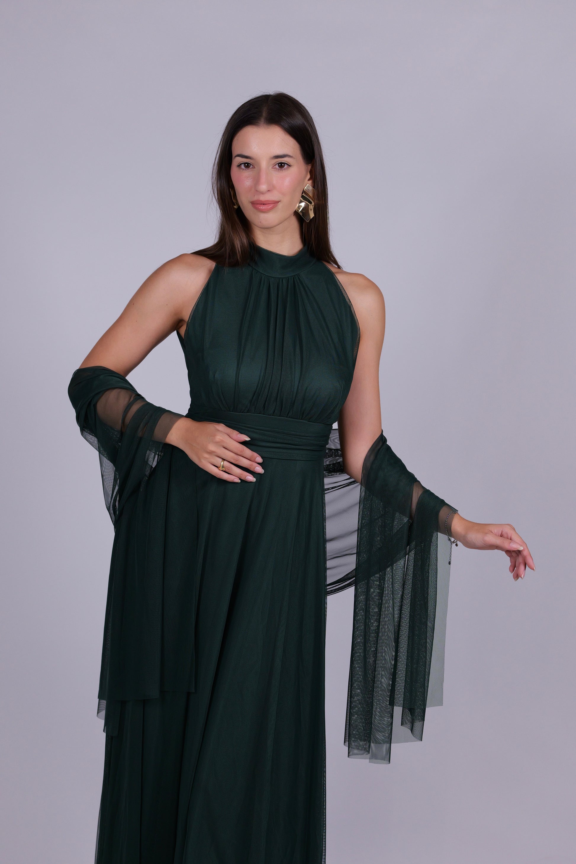 Donna indossa un abito verde scuro elegante, collo a imbarcatura, gonna lunga, con foulard in tulle trasparente, look elegante.