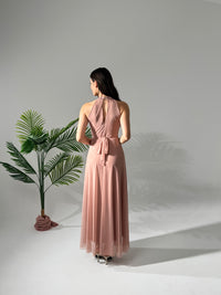 Donna con abito lungo rosa, collo alto a nodo, accanto a pianta
