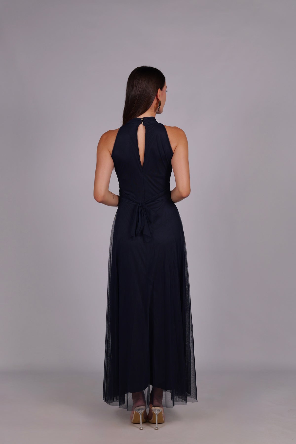 Modella con abito navy a gonna lunga, collo a imbarcatura, foulard in tulle trasparente, outfit sofisticato per eventi.