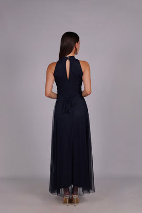 Modella con abito navy a gonna lunga, collo a imbarcatura, foulard in tulle trasparente, outfit sofisticato per eventi.
