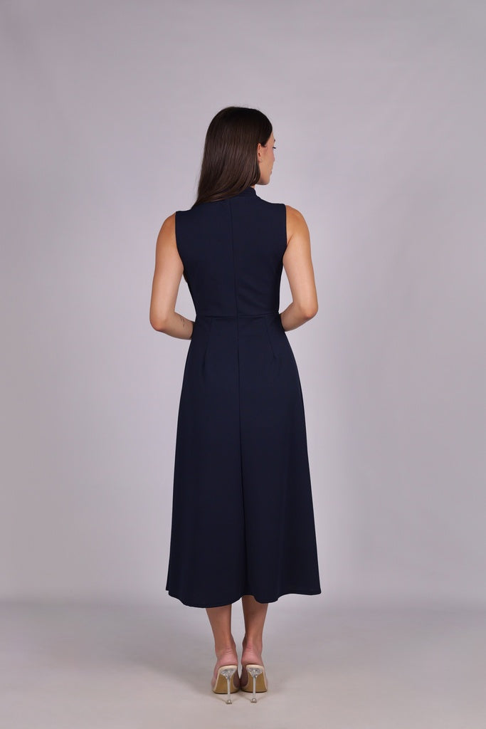 Modella con abito navy a gonna midi, senza maniche, nodo al petto, outfit sofisticato.
