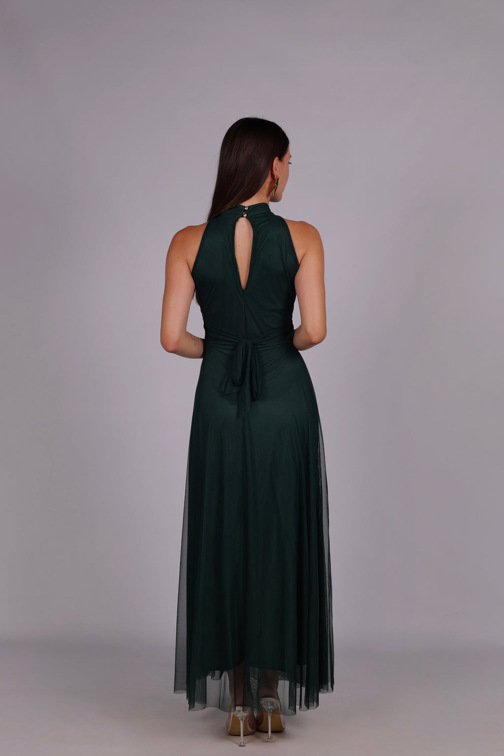 Modella con abito verde scuro a gonna lunga, collo a imbarcatura, foulard in tulle trasparente, outfit elegante per occasioni importanti.