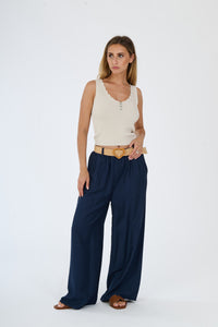 Outfit con top beige senza maniche e pantaloni larghi bianchi, accessorizzato con una cintura in pelle, stile casual e raffinato.