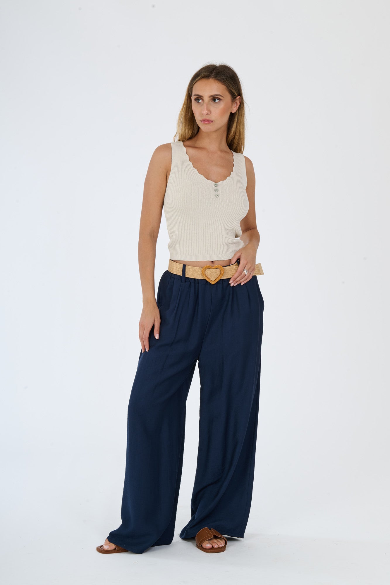 Outfit con top beige senza maniche e pantaloni larghi bianchi, accessorizzato con una cintura in pelle, stile casual e raffinato.