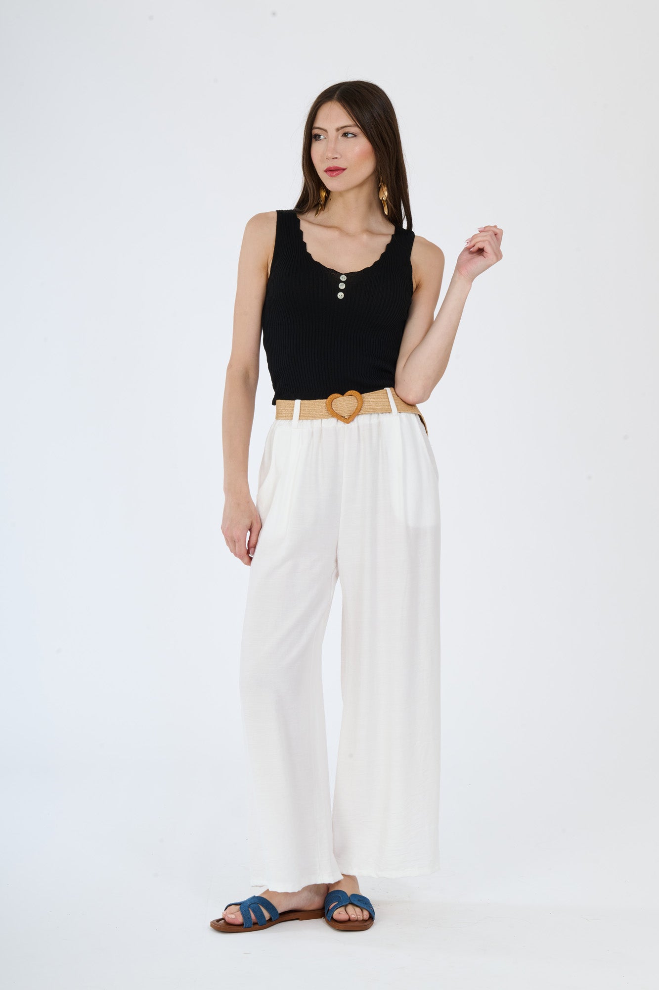 Top nero senza maniche e pantaloni larghi bianchi, abbinamento contrastato con cintura color cammello, stile audace e affascinante.