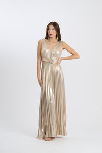 Una donna indossa un abito da sera lungo senza maniche di colore beige con plissé e scollatura a V, su sfondo chiaro.