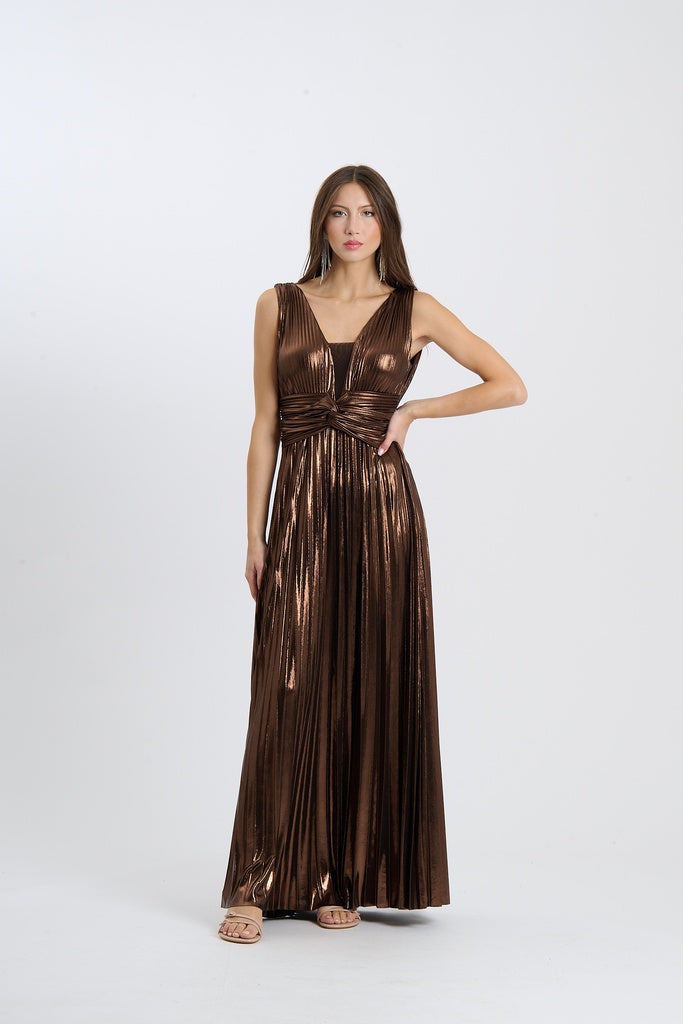 Una donna indossa un abito da sera lungo senza maniche di colore marrone scuro con plissé e scollatura a V, posata su sfondo chiaro.