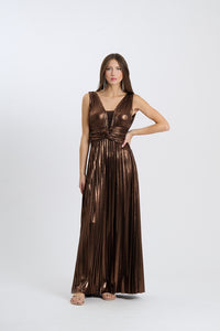 Una donna indossa un abito da sera lungo senza maniche di colore marrone scuro con plissé e scollatura a V, posata su sfondo chiaro.