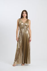 Una donna indossa un abito da sera lungo senza maniche di colore oro con plissé e scollatura a V, su sfondo chiaro.
