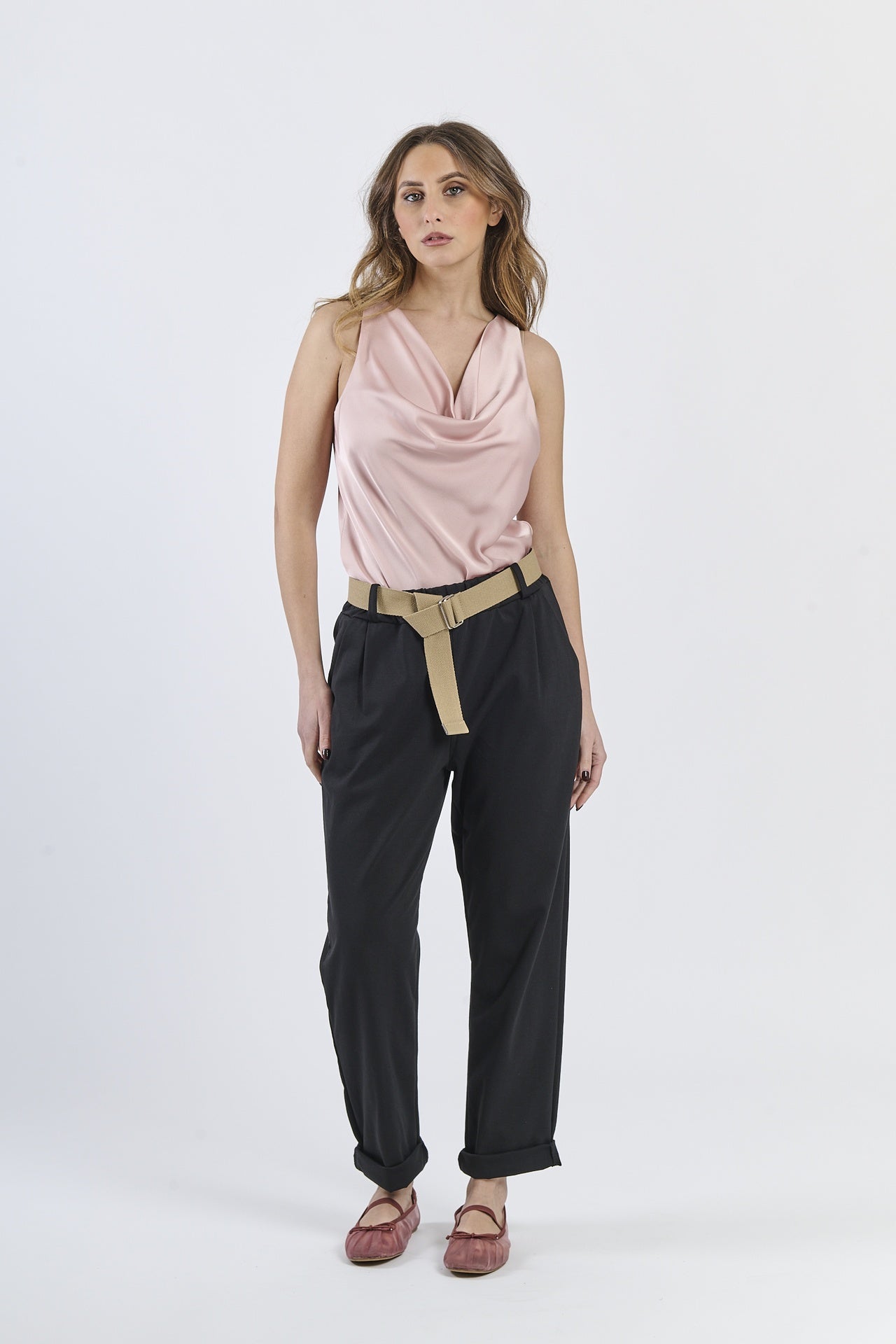 Outfit con top satinato rosa e pantaloni neri, cinghia in tonalità neutra