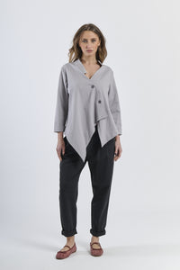 Outfit di camicia grigio irregolare, pantaloni beige avvolgenti e mocassini scuri, eleganza sobria