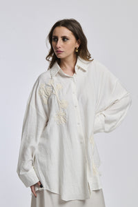 Camicia bianco indossata dalla donna, con un disegno semplice e linee pulite, che sottolinea la sua personalità profonda e riflessiva.