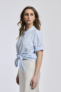 Camicia a righe azzurre e bianche da donna, nodo decorativo sul ventre, perfetta per abbinamenti con gonna larga.