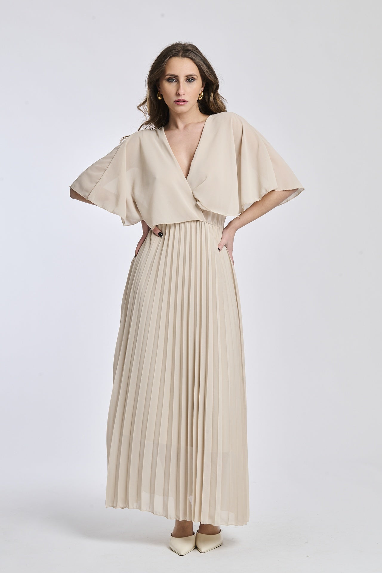 Un abito in beige con lo stesso design crociato e maniche a mantello, creando un'atmosfera di sobrietà e raffinatezza.