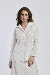 Donna con camicia bianca ricamata, colletto a bottone e orecchini dorati, sfondo bianco