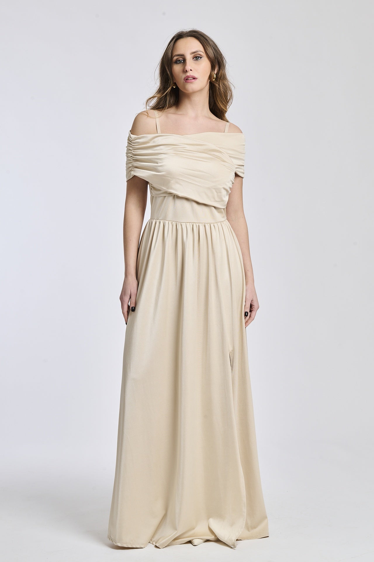 Donna con abito lungo beige, spalline scollate, fascia in vita e apertura laterale raffinata.