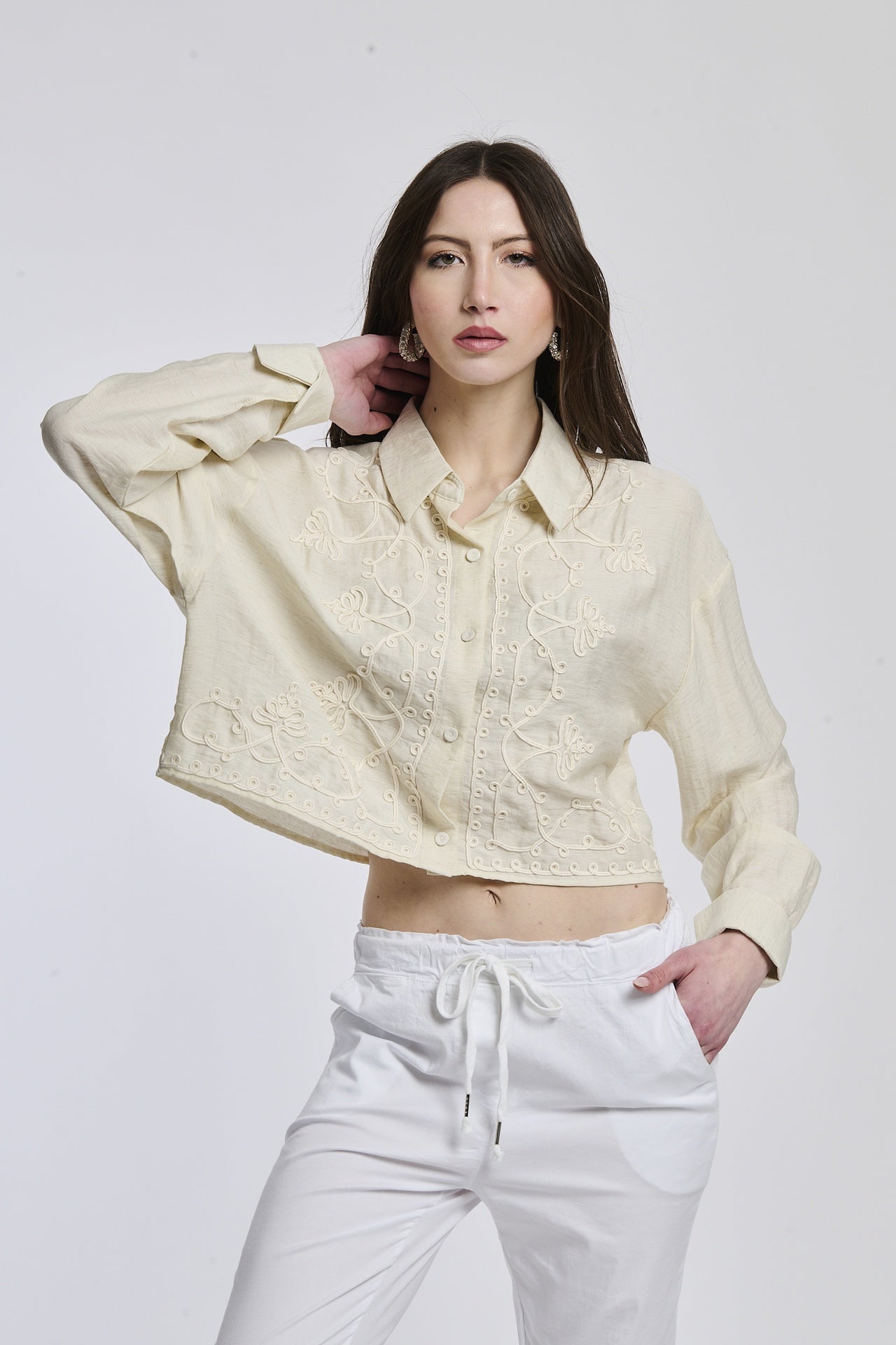 Una donna indossa una camicia a righe blu scuro e bianco, con maniche lunghe arrotolate e un nodo alla vita, esprimendo un’aria di casualità e stile.