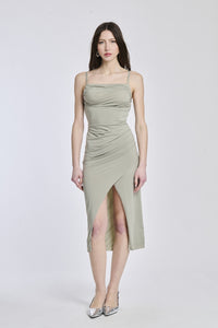 Donna indossa un abito midi salvia, taglio aderente, spalline sottili e sfilo che dona un’aria sofisticata.