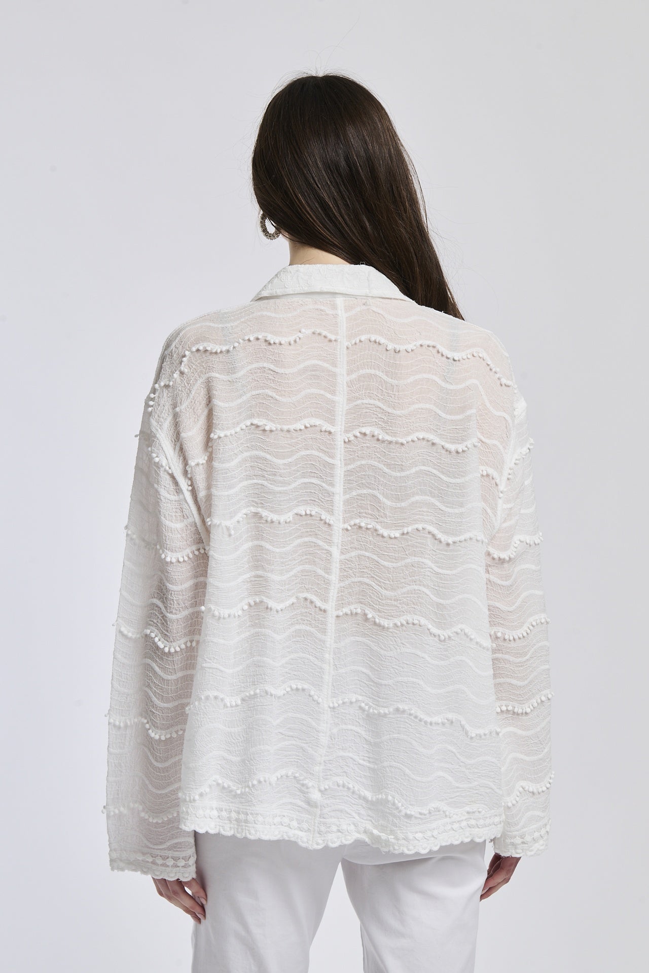 Camicia a maniche lunghe bianco con texture ricamata, abbinata a pantaloni bianchi, sfondo bianco