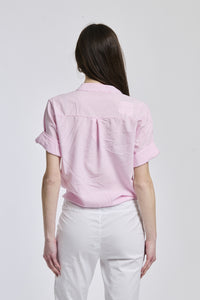 Donna con camicia a righe rosa, maniche lunghe e nodo laterale, ideale per un look romantico.