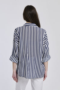 Donna indossa una camicia a righe navy, maniche lunghe e tasca decorativa, stile preppy e raffinato.