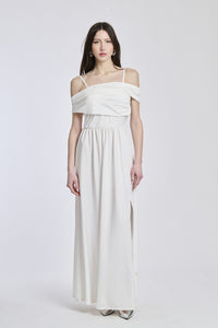 Donna indossa un abito lungo bianco, spalline scollate, fascia in vita e apertura laterale stilosa. 