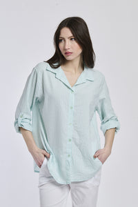 Donna indossa una camicia a righe Tiffany, oversize, colletto a camicia, bottoni frontali e maniche arrotolate.