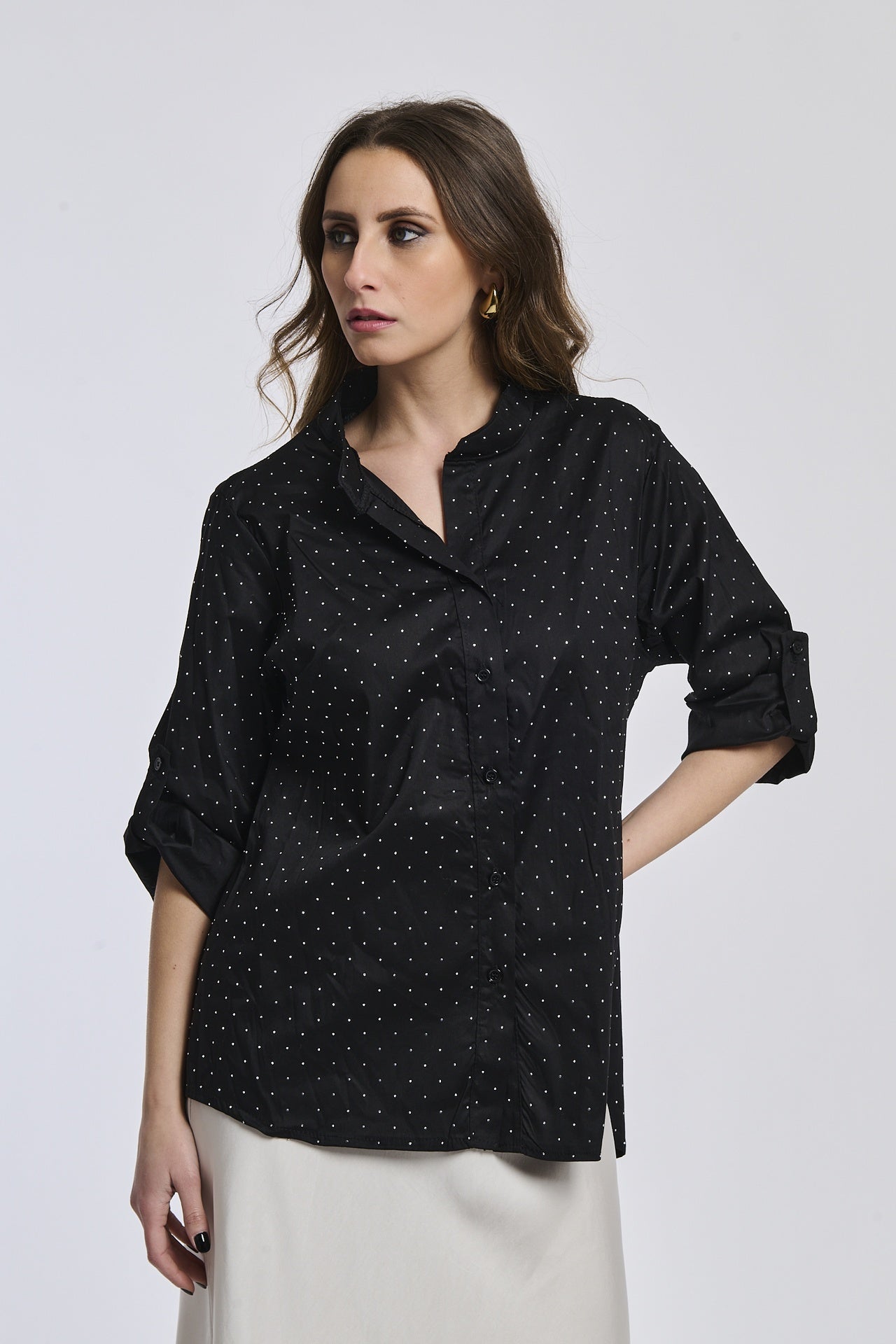 Donna indossa una camicia nera oversize, colletto coreano, bottoni frontali e maniche arrotolate a 3/4.