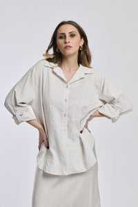 Camicia oversize beige a righe, colletto a V sfiorato, bottoni frontali e maniche arrotolate, perfetta per l’uso quotidiano.