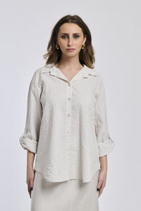 Donna con camicia a righe beige, oversize, colletto a camicia, bottoni frontali e maniche arrotolate.
