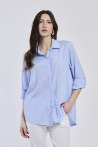 Donna con camicia a righe blu , colletto a camicia, maniche arrotolate a 3/4, taglio oversize.