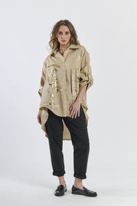 Camicia oversize beige con stampa dorata, abbinata a pantaloni neri