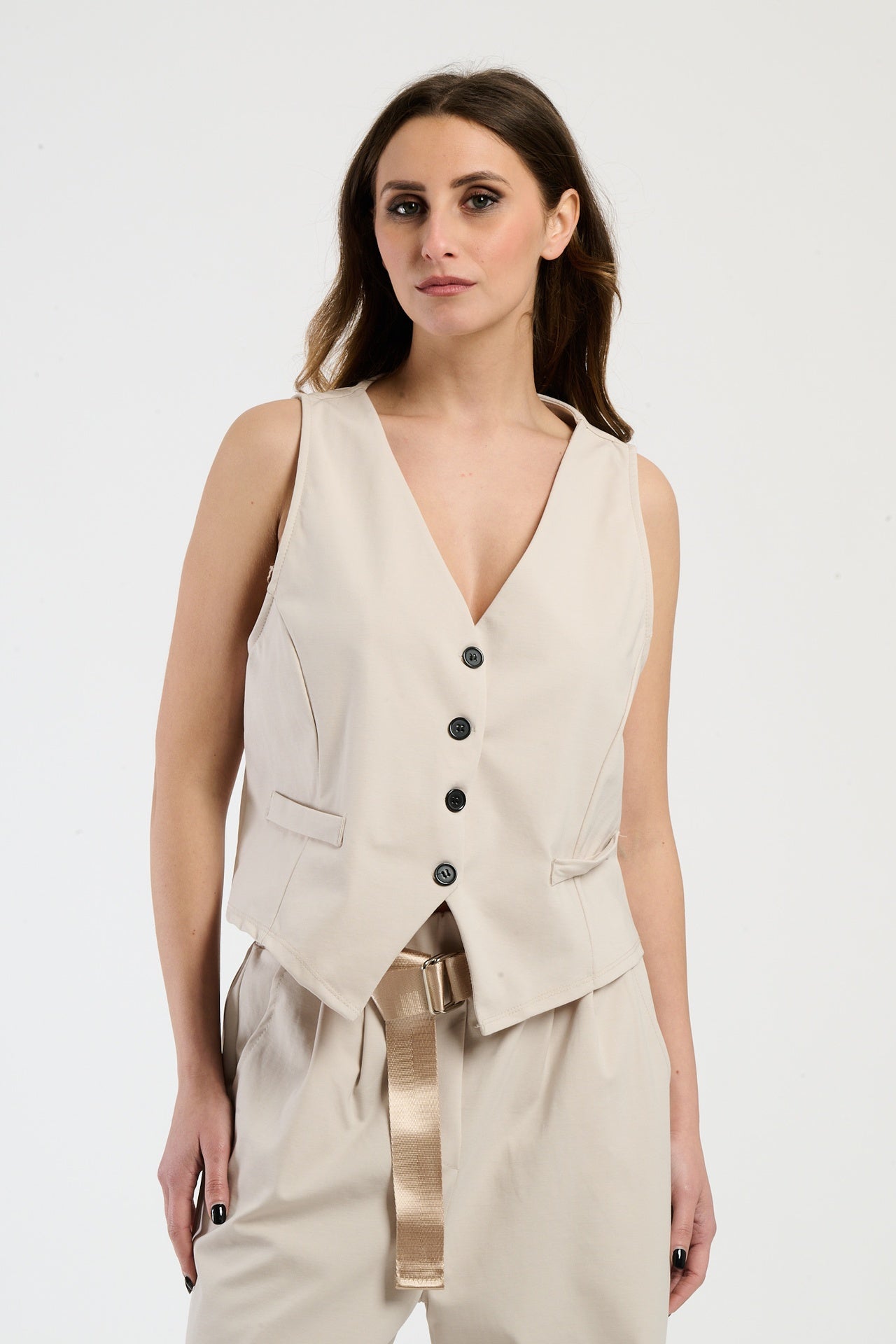 Modella indossa completo beige: gilet senza maniche e pantaloni, stile sobrio e raffinato.