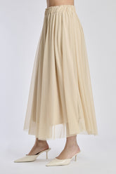 Gonna lunga in tulle beige, vita elastica, abbinata a sandali alti.