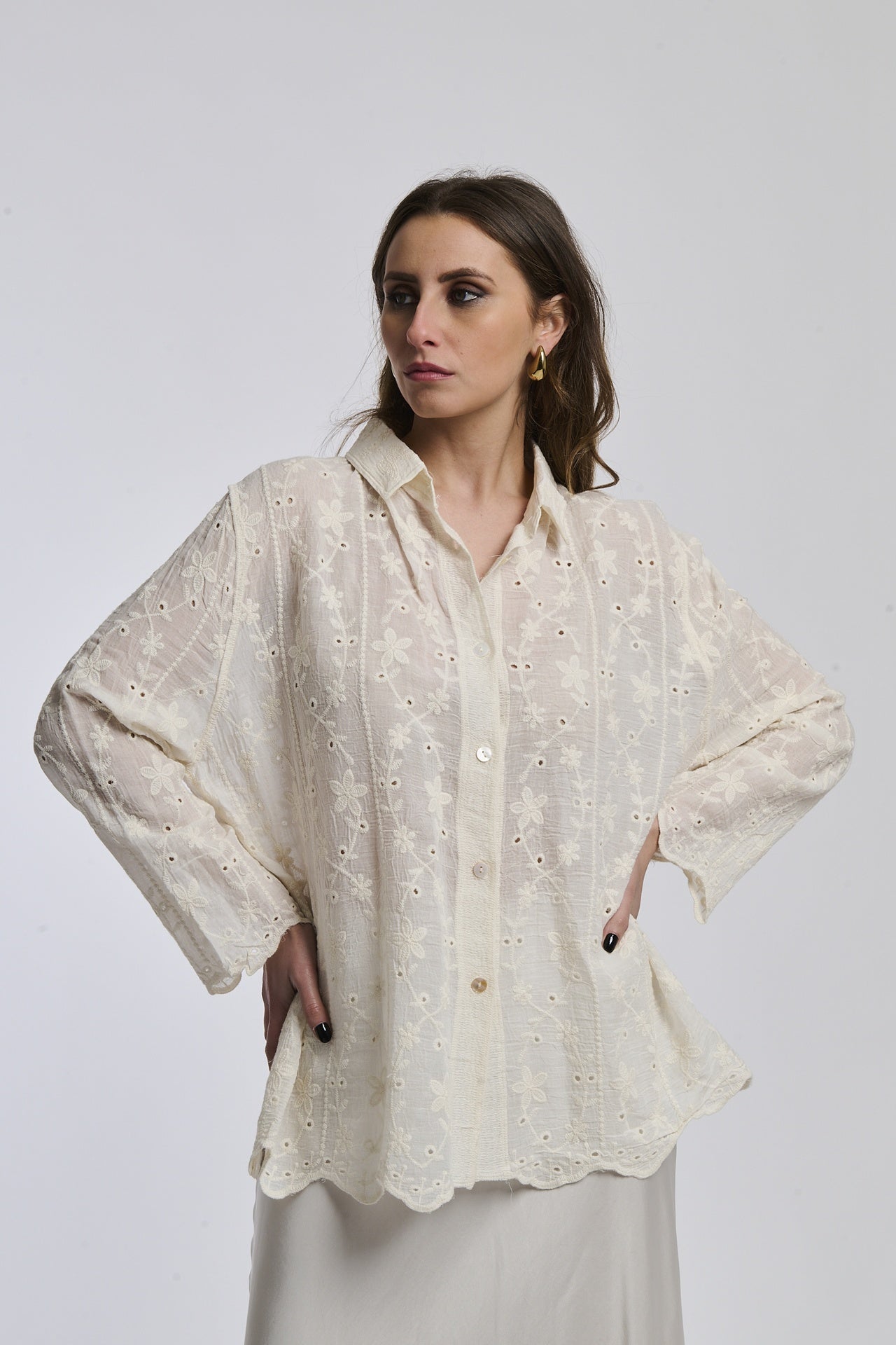 Donna indossa camicia beige a maniche lunghe, colletto a bottone, con dettagli ricamati