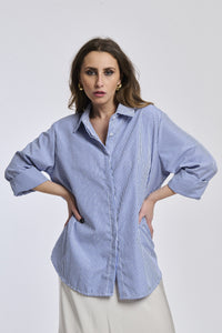 Donna indossa una camicia a righe blu e bianche, colletto a camicia, maniche 3/4
