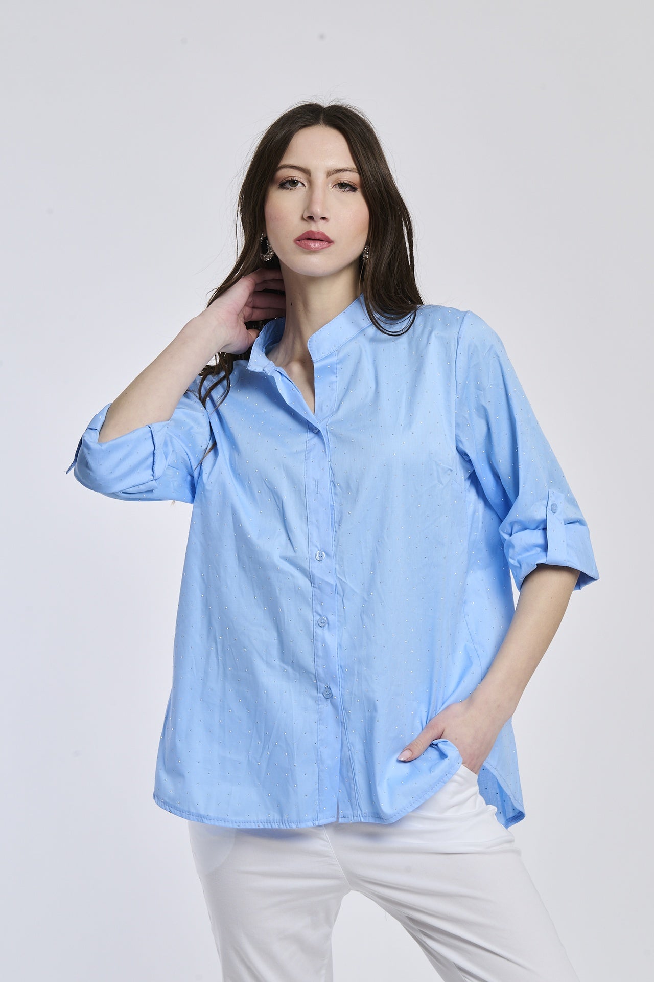 Donna indossa una camicia azzurra oversize, colletto coreano, bottoni frontali e maniche arrotolate a 3/4.