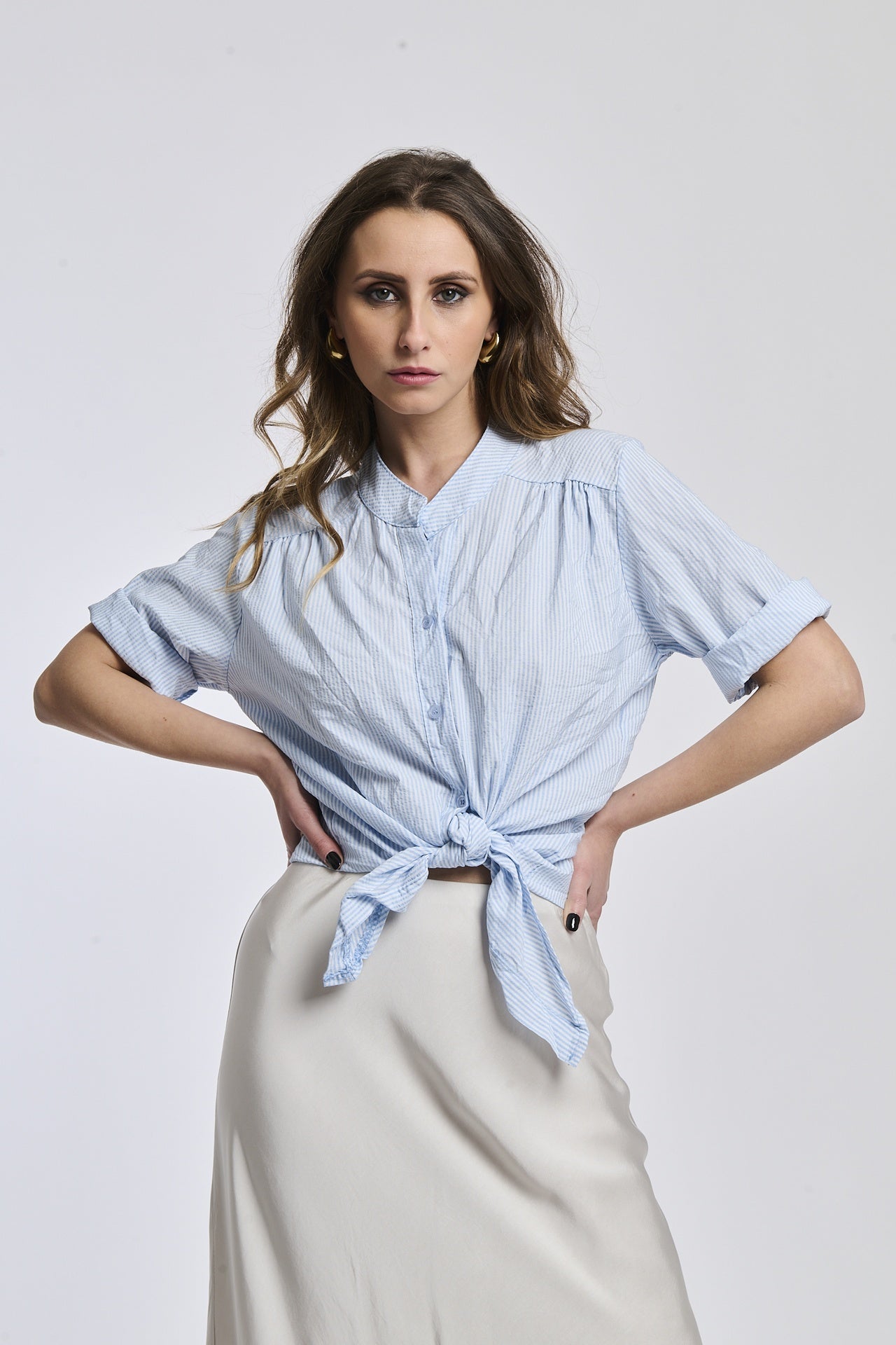 Donna con camicia a righe azzurre, colletto a imbuto e nodo frontale, che conferisce un’eleganza leggera.
